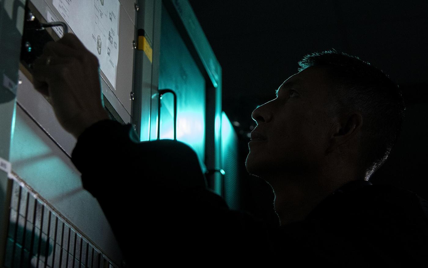 A Satellite Control Network maintainer, in silhouette, works at an equipment rack at Kaena Point Space Force Station